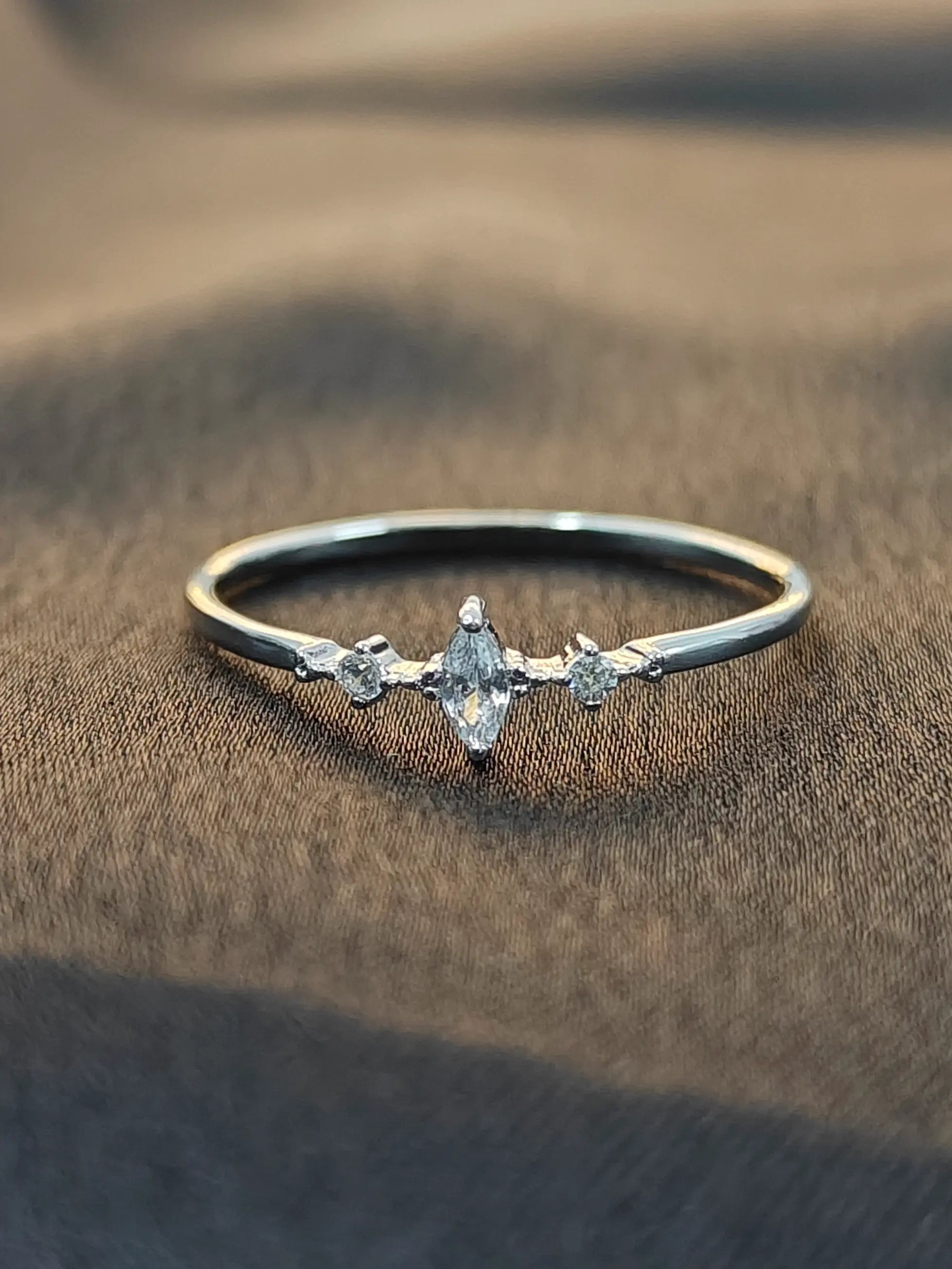 Silver ring with a central diamond and smaller stones on a brown fabric background